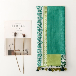 Green bohemian shawl with geometric prints and tassels, displayed on a minimalist background