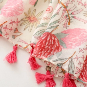 Detail of floral linen scarf with pink blossoms and vibrant fringe tassel accents