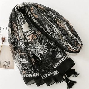 Detail of cotton-linen feel scarf featuring leaf prints, letters, and black tassels