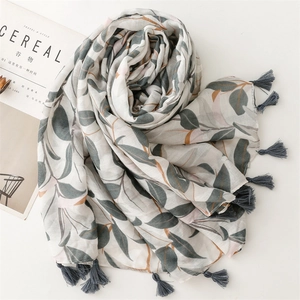 Flat lay di sciarpa effetto lino con motivo a foglie grigio-verdi e nappe accanto a una rivista