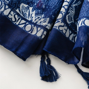 Macro detail of navy cotton-feel scarf showing leaf print, slub texture, and fringe trim