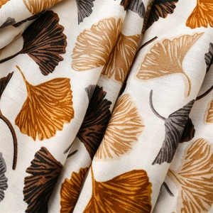 Close-up texture of white cotton linen scarf with orange and brown ginkgo leaf pattern