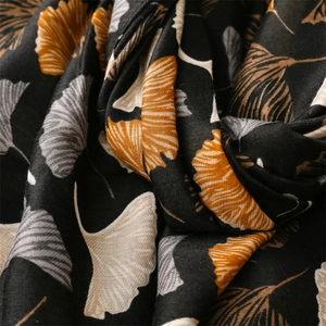 Close-up of soft black linen-feel scarf featuring orange and grey ginkgo leaf patterns