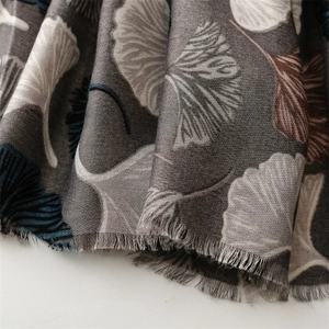 Close-up of dark grey scarf showing white ginkgo leaf pattern and fine fringed edges
