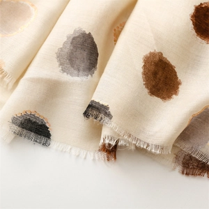 Détail d'une écharpe beige avec des pois dorés et des franges douces sur un tissu texturé