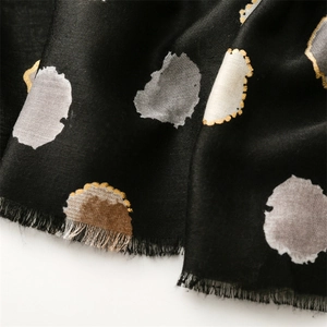 Gros plan d'un foulard noir avec pois dorés, motifs abstraits et bords à franges fines