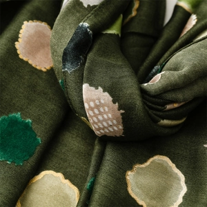 Vue macro d'une écharpe vert foncé avec des pois dorés et une texture en maille fine