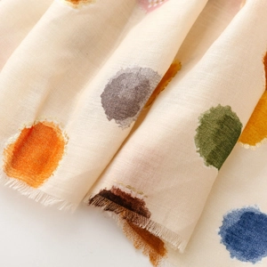 Gros plan d'une écharpe beige avec pois colorés, finition satinée et texture à franges