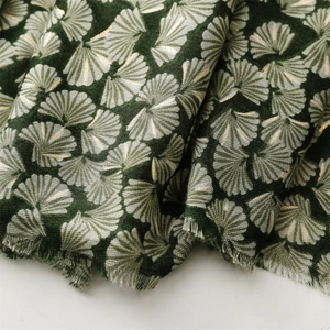 Detail of dark green fabric scarf with gold and white gingko leaf prints and frayed edges
