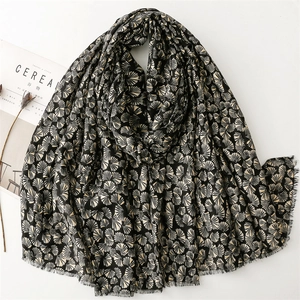 Detailed texture of black scarf with golden ginkgo leaf patterns and fringe edges