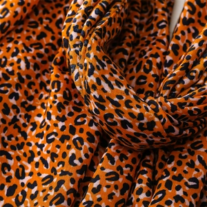 Close-up of leopard print cotton scarf fabric in bright orange with black spot details