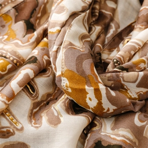 Détail d'une écharpe douce en coton et lin avec motif floral ondulé doré et ourlet roulé