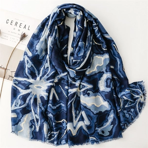 Longue écharpe bleu foncé avec motif floral doré et bords effilochés sur fond blanc