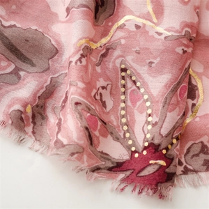 Détail macro d'une écharpe rose avec motifs floraux dorés et texture lin doux