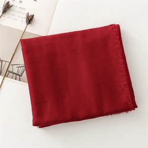 Detail of soft wine red linen-feel scarf with fine fringe edges on a minimalist background