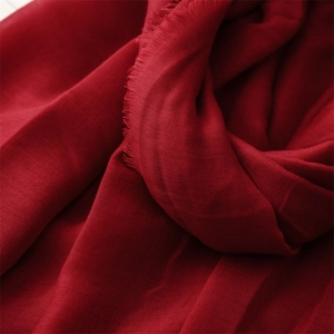 Macro detail of dark red scarf fabric showing delicate fringe and soft woven texture