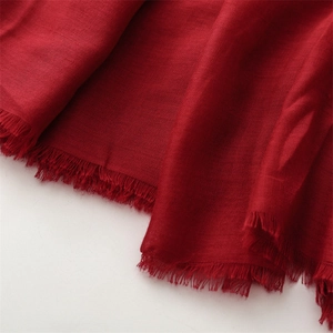 Close-up of deep red shawl fabric texture featuring delicate frayed edges and tassels