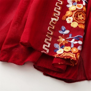 Detailed macro view of colorful ethnic embroidery patterns on a red linen scarf edge