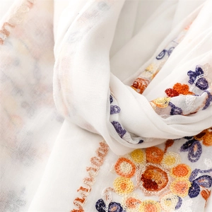 Macro shot of colorful floral embroidery on a white breathable cotton-linen scarf