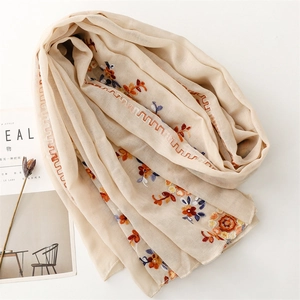 Close-up of geometric floral embroidery and wavy hem on a beige cotton linen shawl scarf