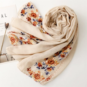 Detail of floral embroidery on a beige linen-feel scarf with wavy scalloped edges