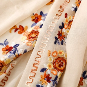 Detail of colorful floral embroidery and wave stitching on beige cotton linen shawl