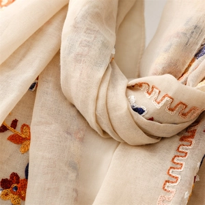 Close-up of ethnic floral embroidery and wave patterns on a beige cotton linen shawl