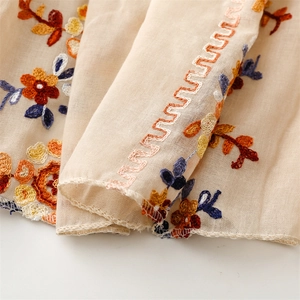 Detail of floral embroidery on beige linen texture shawl with delicate scalloped edges
