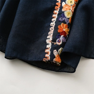Macro detail of navy blue scarf featuring intricate floral embroidery and cotton linen texture