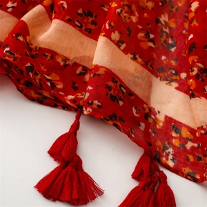 Detail of red floral scarf featuring exotic patterns and handmade woven tassels