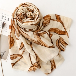 Detail view of beige linen-feel scarf with brown leaf prints and frayed edges on white background