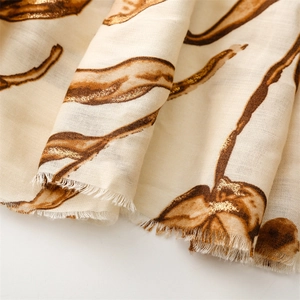 Detail of floral gold foil patterns on beige cotton linen scarf with frayed edges