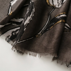 Detailed view of scarf with black leaf print and gold glitter on dark brown fabric