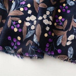 Detail of dark blue scarf with berry print and gold glitter patterns with frayed edges