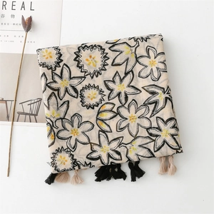 Dettaglio di sciarpa floreale beige con motivi a fiori neri e nappe decorative sui bordi
