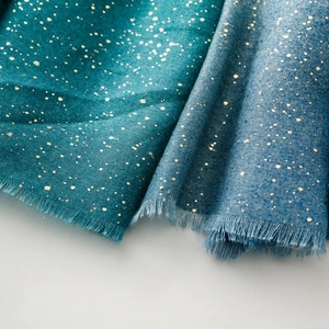 Detailed macro view of gold foil patterns on teal and blue cotton-linen scarves with fringe