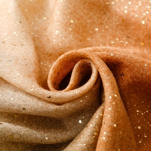 Macro detail of warm orange scarf with fine gold foil texture and shimmering finish