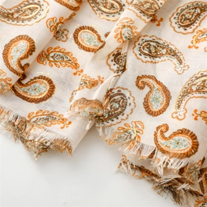 Détail de motifs paisley dorés et franges douces sur une écharpe en coton et lin crème