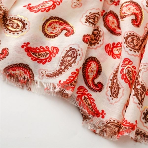 Gros plan du motif paisley doré avec bords effilochés sur une écharpe crème douce