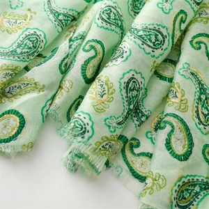 Détail de l'écharpe paisley vert clair avec accents dorés et texture à franges