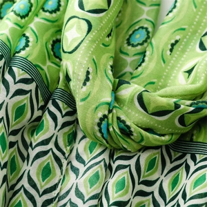 Detailed view of bohemian geometric floral print and fringed texture on green scarf