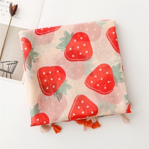 Detail of pink strawberry print scarf featuring decorative orange and white tassels