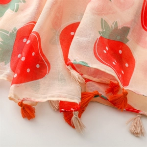 Close-up of strawberry print scarf fabric with orange and beige tassels on the edge