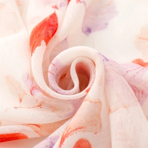 Macro detail of breathable voile scarf featuring vibrant red and orange leaf prints