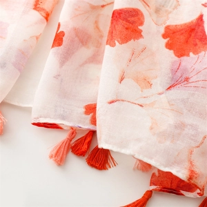 Detailed close-up of ginkgo leaf print and colorful tassel trim on the light scarf