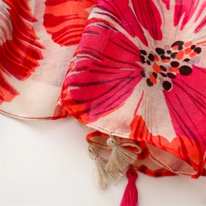 Macro detail of red floral print scarf featuring delicate cotton fabric and handmade tassels