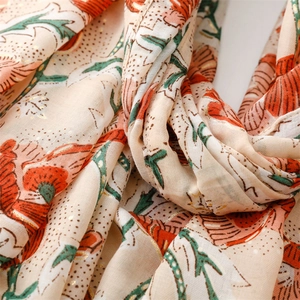 Detail of floral linen-feel scarf showing gold-stamped orange flowers and soft fabric texture