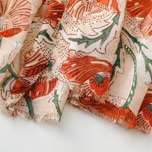 Macro detail of scarf with orange peony print, gold foil accents and frayed edges