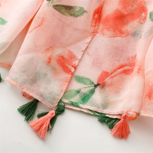 Detail of peach print scarf with fine pink and dark green tassels on semi-sheer fabric