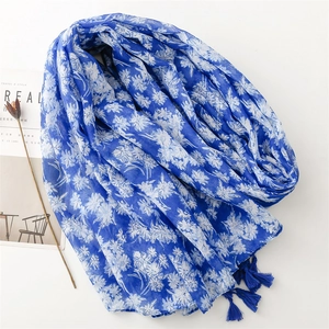 Écharpe bleue aspect coton-lin avec motifs floraux blancs et pompons sur fond blanc pur